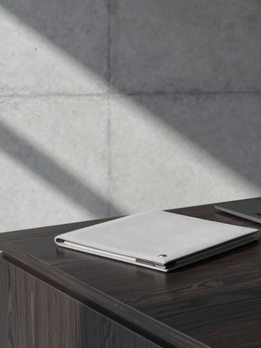 Sharp architectural shadows on a concrete wall, a clean leather folder on a modern dark oak desk, cool overcast daylight, desaturated corporate tones, 50mm lens.