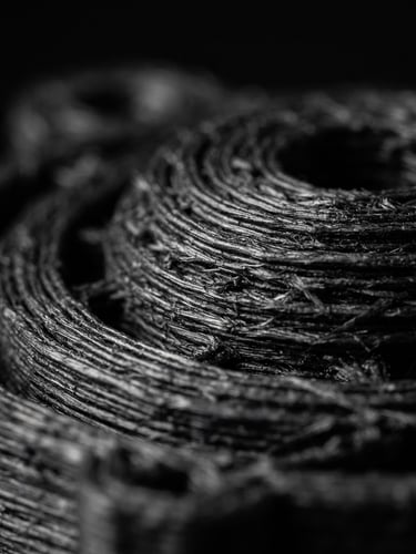 Extreme macro shot of 3D printed carbon-reinforced filament layers, high-contrast studio lighting, dark moody background, sharp details, 35mm