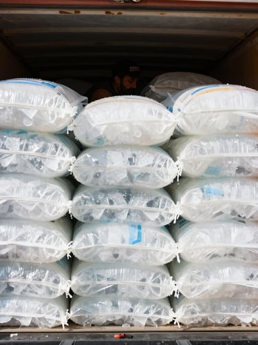 A worker stacking pristine, heavy bags of crystal-clear ice into a delivery truck under bright high-key Egyptian sunlight.