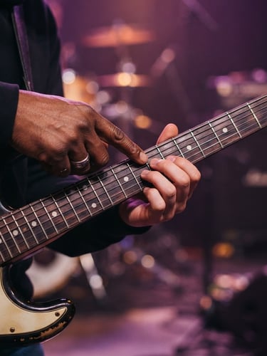 A close-up of a student's hands learning electric guitar frets from an instructor, warm purple stage backlighting, premium editorial photography style.
