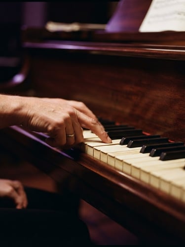 A close-up of hands guiding a student's fingers on a polished mahogany piano, warm studio lighting with subtle purple backlights, rich deep tones, shallow depth of field, 85mm lens