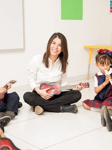 Teacher sitting with students in a classroom music circle.