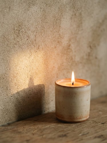 A close-up of a lit candle casting a soft, warm golden shadow on a textured beige wall, minimalist styling, warm editorial photography