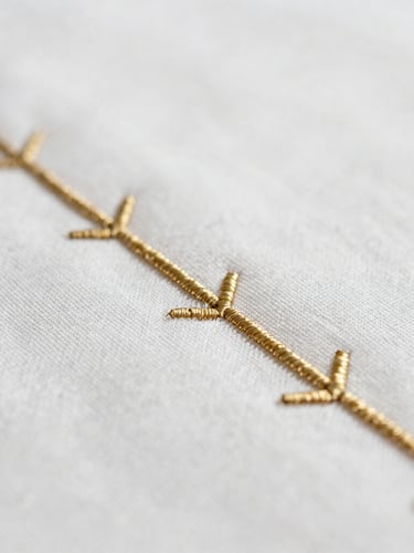 Extreme close-up of gold-embossed embroidery on pristine white linen, macro photography, shallow depth of field, soft natural light