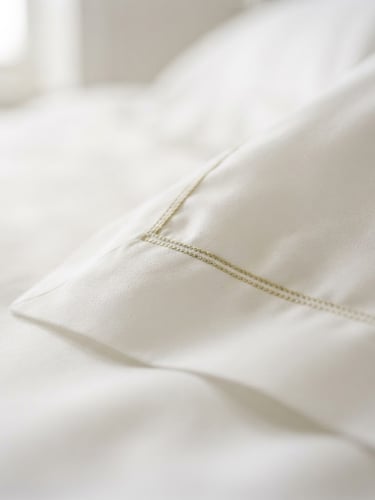 Editorial luxury photography, extreme close-up of crisp white 500 TC cotton bed linen, soft natural daylight, shallow depth of field, minimalist elegant setting