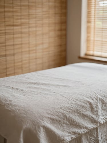 Macro detail of warm, natural light filtering through bamboo blinds onto a clean linen-draped massage table, soft editorial photography, muted earth tones, minimalist composition, shallow depth of field, 35mm