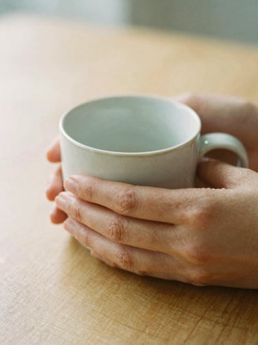 A close-up of hands holding a warm ceramic mug on a wooden table, soft diffused morning light, shallow depth of field, calming tones