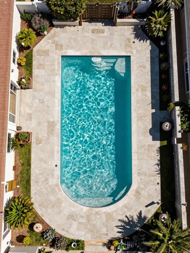 Overhead drone perspective of a residential pool in a coastal Southern California neighborhood at midday, aquamarine water surface immaculate, surrounding patio clean, mature landscaping visible at edges, no people