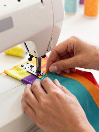Close up of artisan hands carefully stitching a colorful pet fabric on a sewing machine in a bright, warm workshop in Celaya, natural light, 35mm