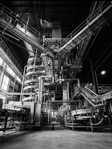 Low-angle heroic perspective of a modern automated food processing facility, high contrast black and white with dramatic side-lighting