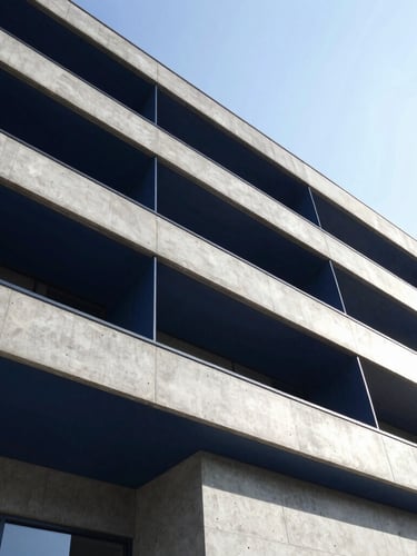Low-angle architectural photography of a modern concrete and steel building facade, sharp geometric angles, bright daylight with high contrast, deep navy and steel tones