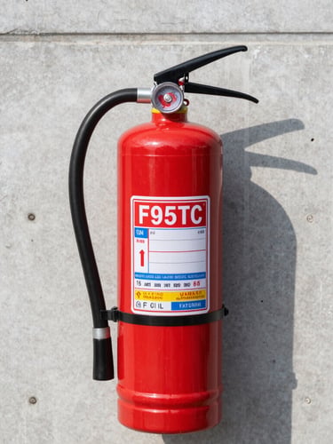 Close-up of a bright red commercial fire extinguisher mounted on a clean industrial concrete wall, crisp daylight, sharp focus on the pressure gauge showing full charge