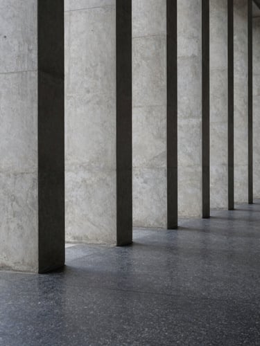 Minimalist architectural shot of tall, vertical concrete columns casting long, geometric shadows on a dark granite floor, soft overcast natural light, clinical precision.