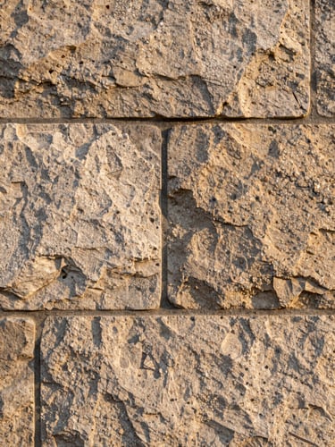 Close-up of a dressed stone wall section with a recessed mortar joint, raking afternoon light exposing surface texture and mineral grain, no people, architectural detail only