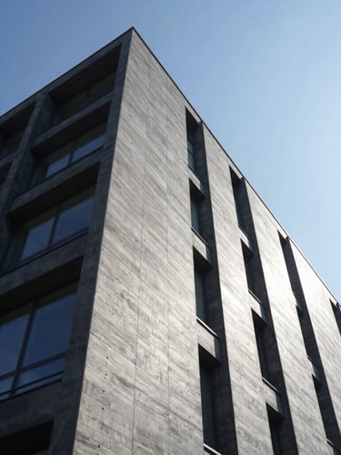 Low-angle sharp architectural photograph of a modern steel and concrete building facade under bright crisp daylight, high-contrast shadows, clean structural lines, slate gray tones
