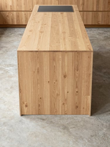 Straight-on architectural photograph of a finished minimalist oak kitchen island meeting a raw concrete floor, sharp daylight, 35mm