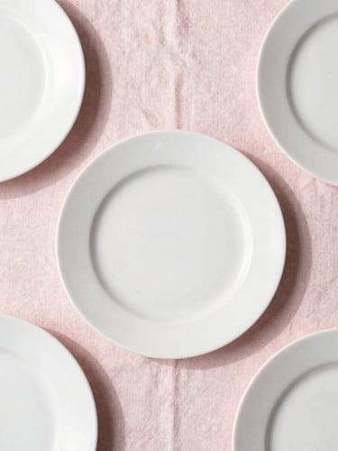 Overhead flat-lay of a minimalist table setting with soft blush pink linens, delicate white plates, and natural daylight casting gentle shadows, 35mm