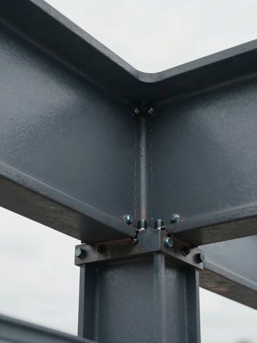 Close-up of a heavy structural steel beam connection point, high-strength bolts and weld seams under bright overcast light, sharp industrial detail, charcoal-gray surface finish