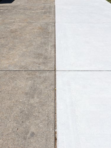 A sharp split-screen before-and-after shot of a concrete driveway, one side dark with years of dirt, the other side brilliant clean white concrete under bright direct sunlight, 35mm lens.
