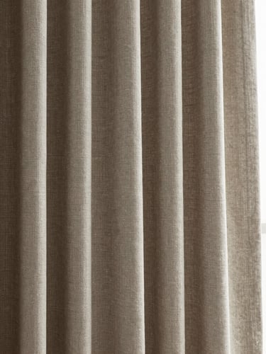 A close-up of a floor-to-ceiling custom linen curtain hanging in soft, deep folds, natural side-light from a window casting delicate shadows on the heavy weave