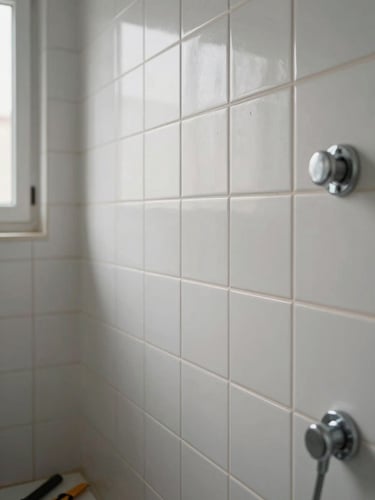 Close-up environmental shot of a freshly tiled bathroom wall in a Seville apartment — clean grout lines, matte ceramic tiles, a chrome fixture being installed at the right edge, overcast natural light from a nearby window, no people visible, tools resting on the floor in the lower corner