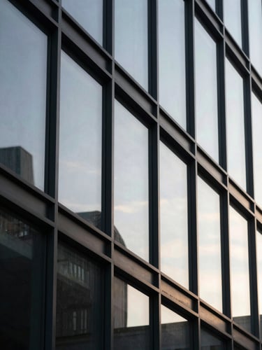 Close-up of modern architectural glass reflecting soft morning sun, clean minimalist lines, low-contrast natural light, cinematic framing.