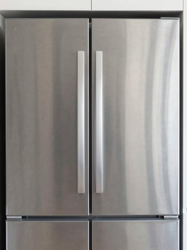 Straight-on architectural crop of a brushed-steel refrigerator integrated into a modern kitchen, soft side-light, sharp focus on metallic seams, 50mm lens.