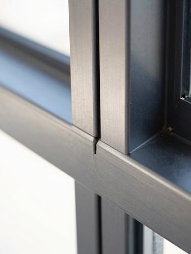 Extreme close-up architectural photography of a flawless aluminum miter joint on a dark anodized charcoal frame, sharp metallic reflections, bright harsh daylight, high contrast.