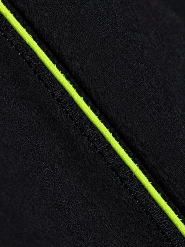 Macro close-up of high-tension flatlock stitching on black moisture-wicking athletic fabric, neon volt thread details, dramatic studio side lighting showing fabric texture