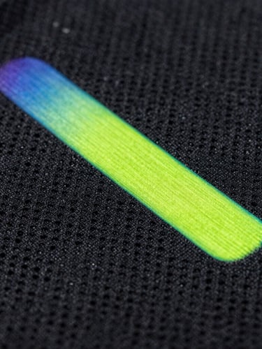 Extreme close-up of neon volt sublimation ink fusing into black athletic fabric, showing the intricate moisture-wicking pore structure.
