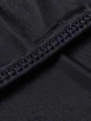 Extreme macro close-up of high-tension flatlock stitching on a matte black athletic jersey, showing the intricate technical thread weave under sharp rim lighting.
