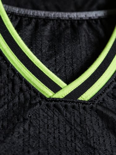 Macro close-up of heavy-duty tackle twill stitching on a black basketball jersey, dramatic neon volt rim lighting, professional athletic texture