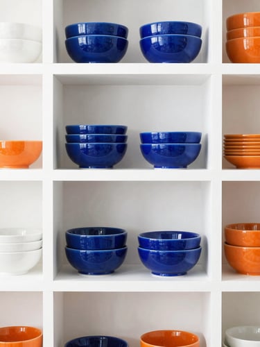 Straight-on clean shot of beautifully organized retail shelves with curated ceramic home goods, bright high-key natural lighting, sharp focus, white background, orange accents.