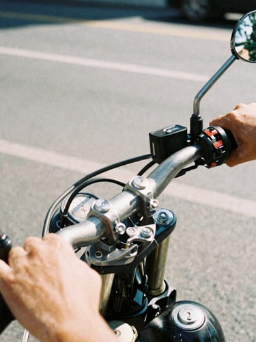 Close-up of hands on motorcycle handlebars, gritty urban street background, daylight, high-contrast warm tones, 35mm