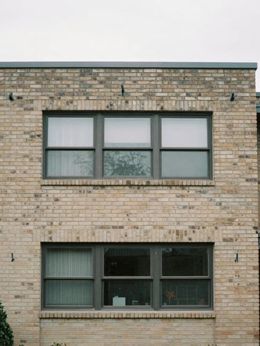 Straight-on architectural framing of a mid-century brick residential elevation, natural overcast daylight, desaturated neutral tones, sharp focus, 35mm