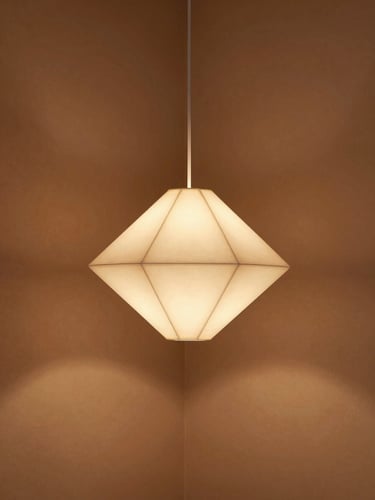 A lit origami pendant lamp hanging in a minimalist Japandi room with warm clay walls, casting soft, layered geometric shadows, cozy evening light.