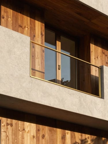 Close-up architectural detail of a premium residential facade, showing textured white concrete, warm wooden panels, and polished brass accents under sharp sunlight.