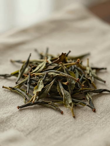 Close-up overhead environmental shot of loose tea leaves resting on textured linen, soft diffused morning light, warm earthy tones, 35mm.