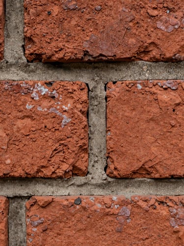 Macro detail of weathered historic red brickwork with deeply recessed mortar joints, natural overcast daylight emphasizing the rough clay texture, sharp focus on central brick edge.