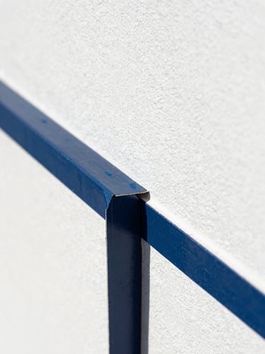 Macro close-up of a sharp paint tape line being pulled away to reveal a flawless, crisp navy blue edge on a bright white stucco wall under intense Florida sun.