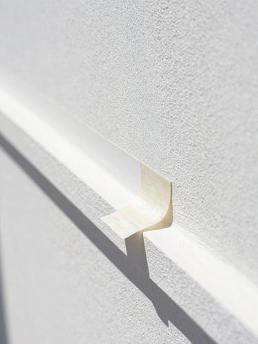Macro detail shot of a crisp paint tape line being pulled back, revealing an immaculate sharp edge on a white stucco wall under bright Florida sun.