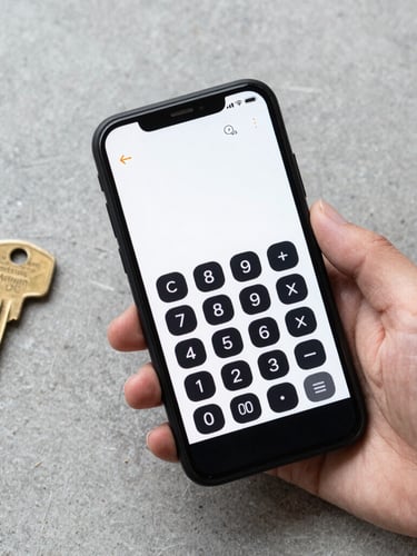 Top-down flat lay of a matte black Android phone held in a hand, displaying a clean black-and-white calculator interface, resting on a light gray concrete desk beside a brass key.