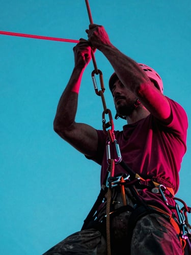 Low-angle heroic shot of a professional tree climber's hands knotting heavy rigging ropes, carabiners and climbing harness visible, high-contrast twilight with cyan ambient fills, 35mm