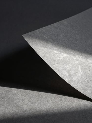 A high-contrast chiaroscuro still life of textured handmade paper catching soft silver moonlight, casting deep architectural shadows, minimalist composition.