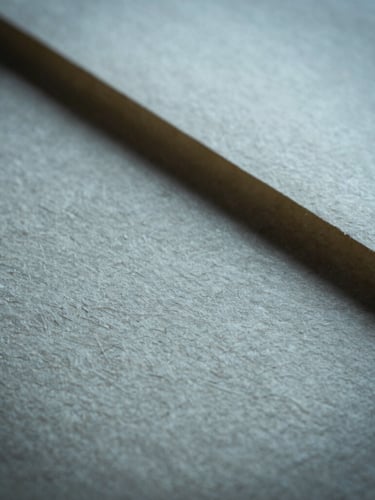 A close-up macro shot of heavily textured handmade paper catching soft, cool raking light, casting deep shadows