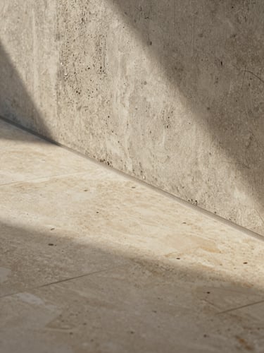 Macro architectural photograph of a flawless transition between a polished travertine floor and a textured raw concrete wall, soft golden light