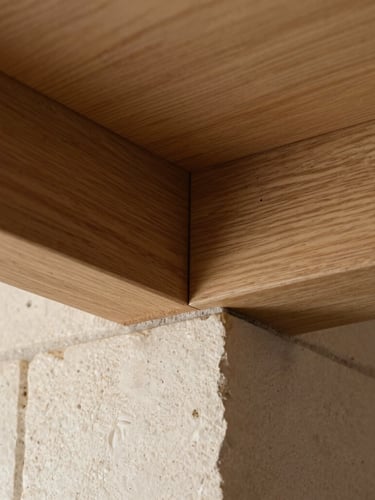 Close-up of a perfectly executed structural joint, raw oak beam meeting textured light stone under natural side-lighting.