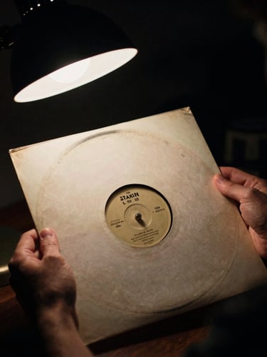 A collector's hands carefully holding a vintage 12-inch vinyl sleeve, soft analog glow from a desk lamp, moody low-key studio lighting, rich dark tones, 35mm film grain