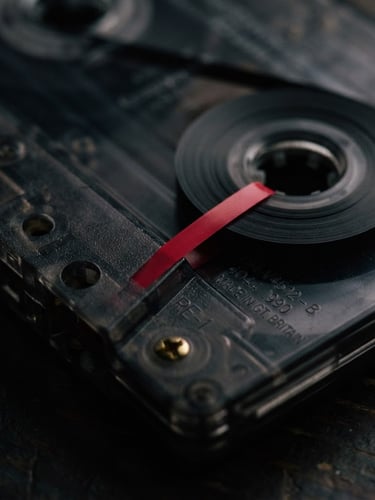 Macro close-up of a physical Depeche Mode cassette shell, showing detailed matrix numbers and red leader tape under moody low-key lighting, deep shadows, 35mm film grain