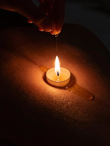 Intimate close-up of warm oil being gently poured onto skin under flickering candle light, casting deep shadows, rich amber glow, moody low-key photography.
